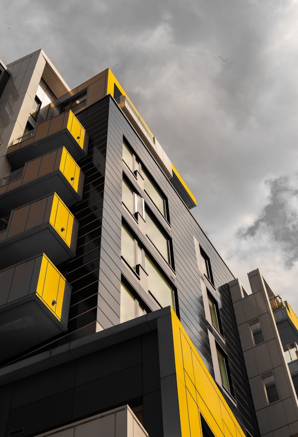 Modern apartment building with yellow balconies under a cloudy sky.